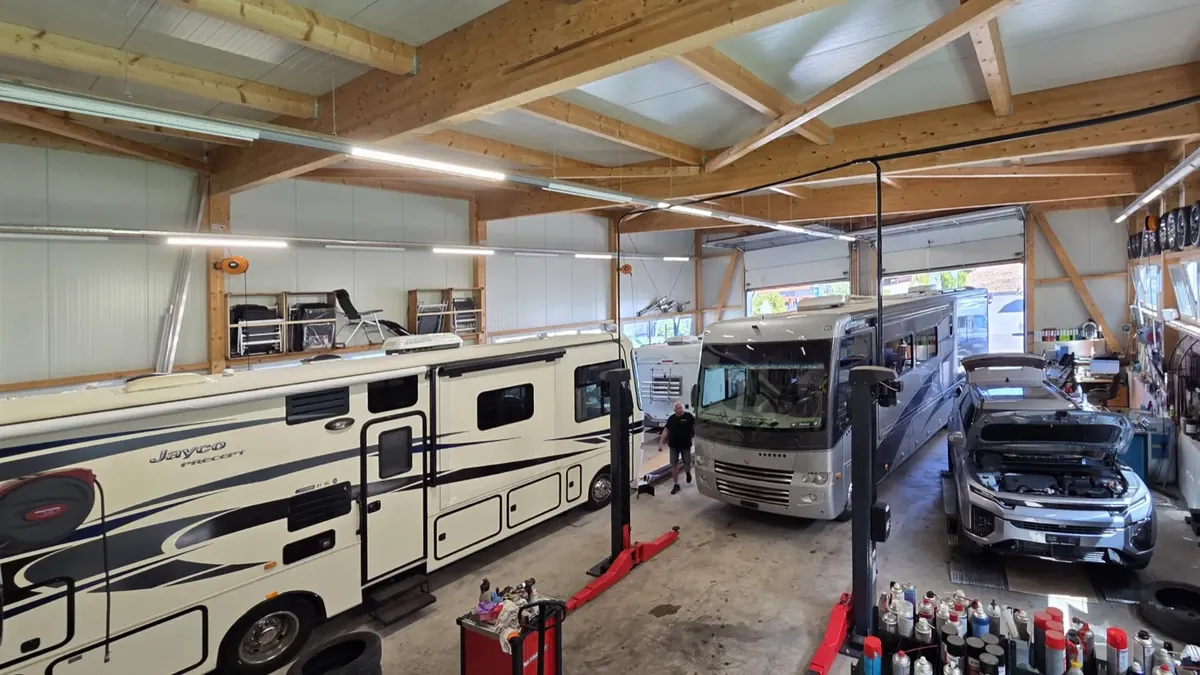 Werkstatthalle mit zwei amerikanischen Wohnmobilen, einem Alkoven-Wohnmobil und einem Personenwagen auf den Reparaturplätzen